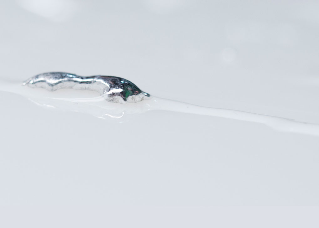 A slug-like shaped blob of silvery liquid metal with clear atom thick trail.