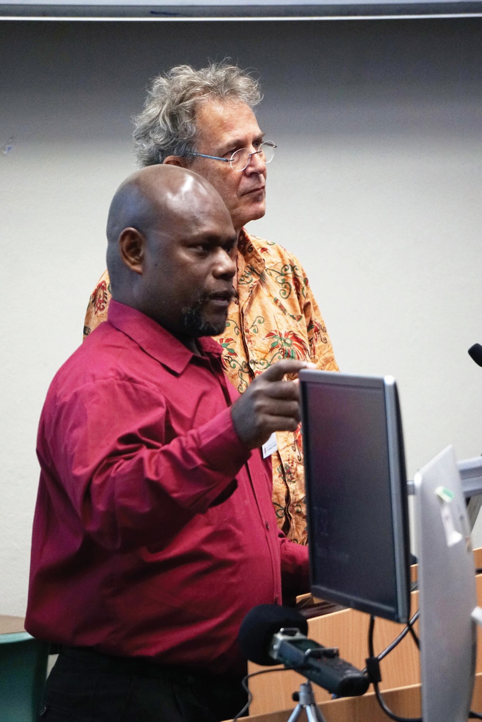 Professor Nick Evans and Dr Alpheaus Graham Zabule standing at lectern with computer monitor, giving a presentation within a lecture theatre. 