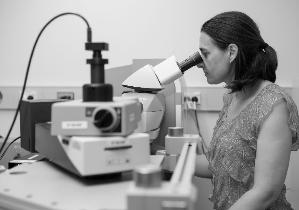 Black and white photograph of Associate professor Jodie Bradby looking through a microscope.