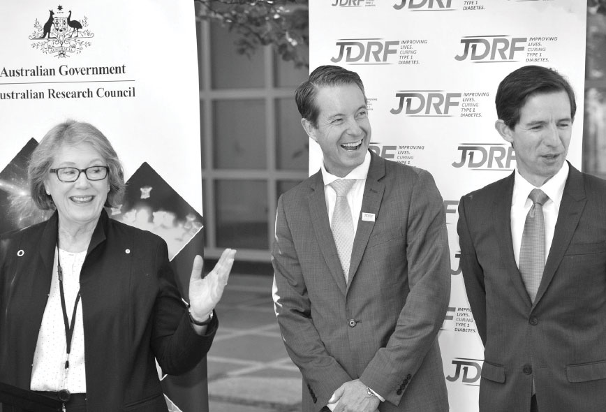 Black and white photograph of Ms Judi Moyan, Mr Mike Wilson and Senator the Hon. Simon Birmingham standing in front of a Juvenile Diabetes Research Foundation sign.