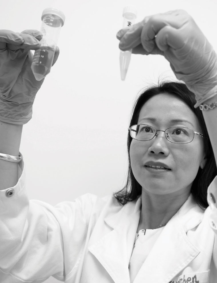 Black and white photograph of Associate Professor Guozhen Lieu holding up test tubes.